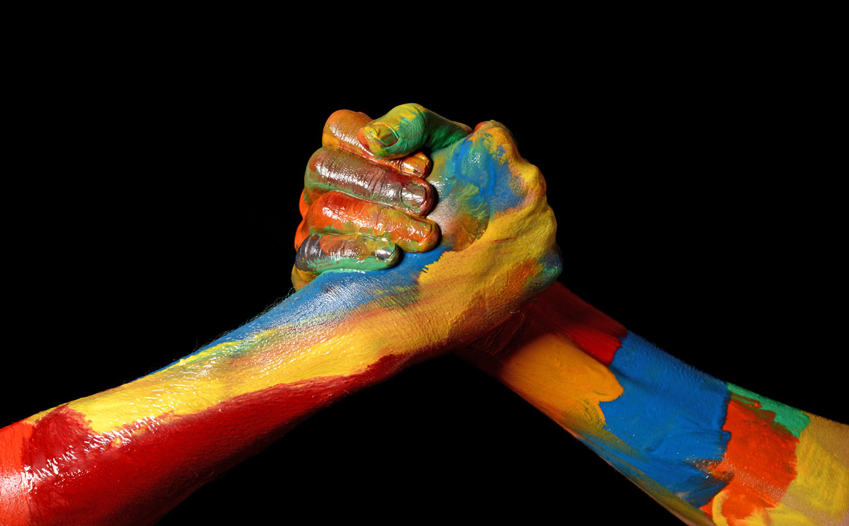Stock photo of two clasped hands covered in brightly colored paint.